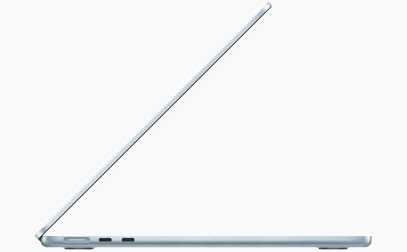 A sleek, silver laptop partially open, viewed from the side. It has a minimalist design with a thin profile, showing two USB-C ports on the left edge. The device's screen is slightly tilted back, revealing its modern and simple aesthetic.