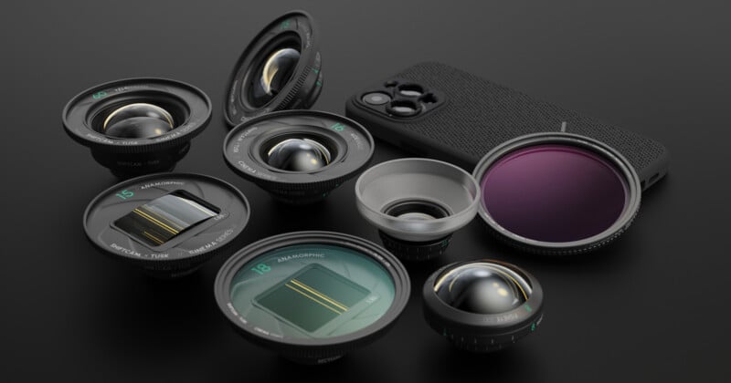 A collection of camera lenses of various shapes and sizes arranged on a dark surface next to a smartphone with a textured back. The lenses have different designs and colors, and the phone has a large camera module.