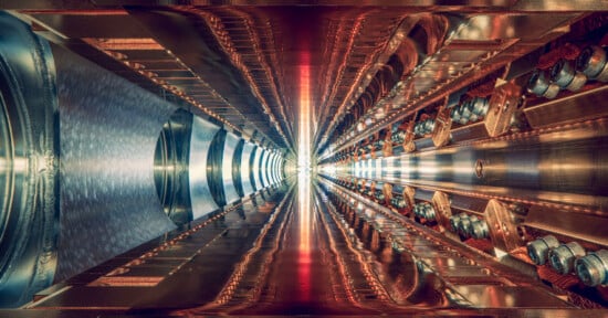 A futuristic, symmetrical corridor with metallic, intricate machinery on both sides. The perspective creates a tunnel effect, with a bright light at the center, highlighting the complexity and detail of the components.