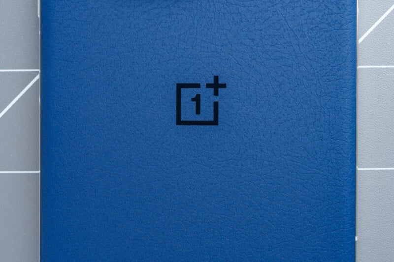 Blue textured surface with a black logo featuring a stylized square and the number "1" followed by a plus sign. The background shows a grid pattern with intersecting lines in light gray tones.