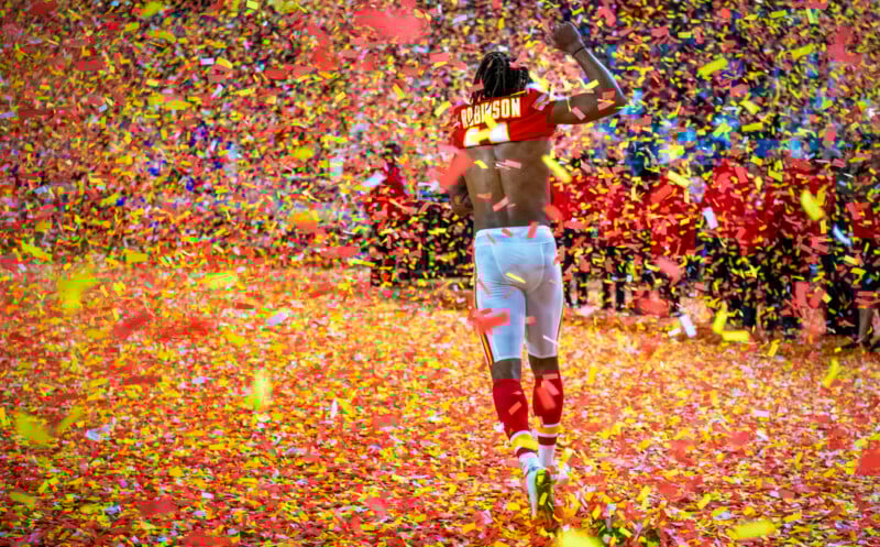 Football player in a white jersey with red and yellow details walks away on a field covered in vibrant red and yellow confetti. The crowd is celebrating in the background, adding to the festive atmosphere.