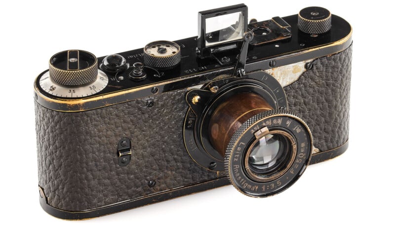 A vintage black Leica camera with a textured body and a prominently attached lens. The camera features multiple dials and a viewfinder, showing signs of wear with some faded areas, indicating its age and frequent use.