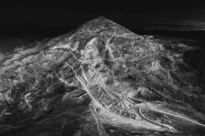 Aerial black and white view of a mountain with winding paths and roads carved into its slopes, set against a dark sky.