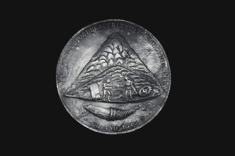 An ancient coin featuring a raised design of a mountain with clouds above it. Two figures are depicted mining with a bag and tools. Spanish text encircles the edge, and the year 1651 is inscribed at the bottom against a black background.