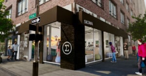 Street view of a Sigma store on a city corner, featuring a black and white modern exterior. People walk by and stand near the entrance. Large windows display camera equipment inside. Street signs read Spring and One Way. Sunlight illuminates the scene.