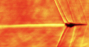 An infrared image of a jet forms a blurry zigzag pattern through the air, with bright orange and red tones indicating heat. The aircraft is in silhouette against the heated background.