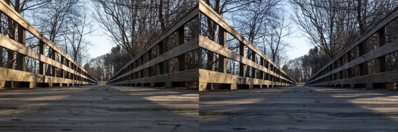 Low-angle view of a wooden bridge surrounded by leafless trees on both sides. The bridge leads into a wooded area under a clear blue sky. The wood planks are weathered, and the perspective adds a sense of depth.