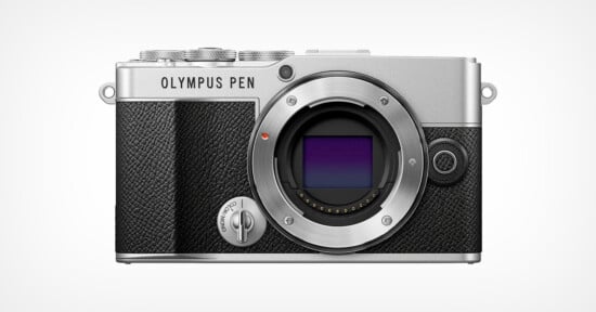 A front view of an Olympus PEN camera body with a vintage design. The camera is silver with black textured grips. The lens mount is exposed, showing the sensor. The camera features dials on the top for adjustments.