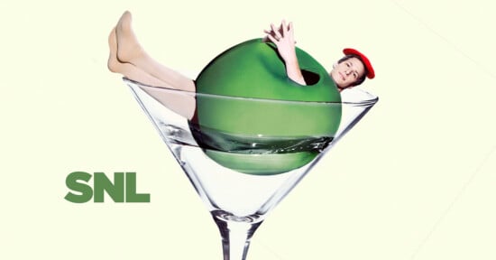 A person wearing a red beret playfully emerges from a large green olive in a martini glass. The background is light, and the "SNL" logo is at the bottom left.