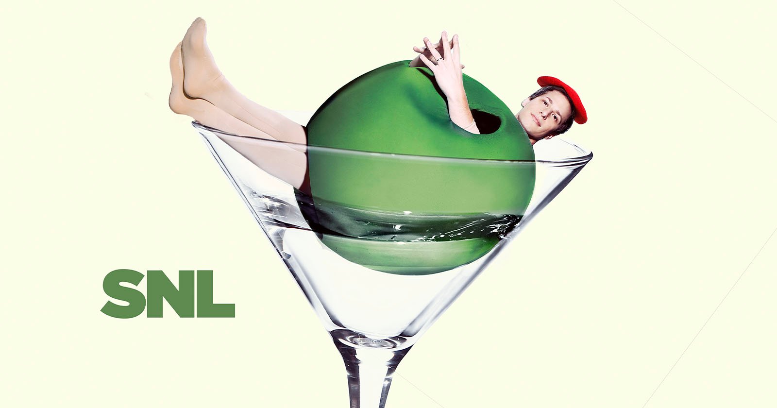 A person wearing a red beret playfully emerges from a large green olive in a martini glass. The background is light, and the "SNL" logo is at the bottom left.