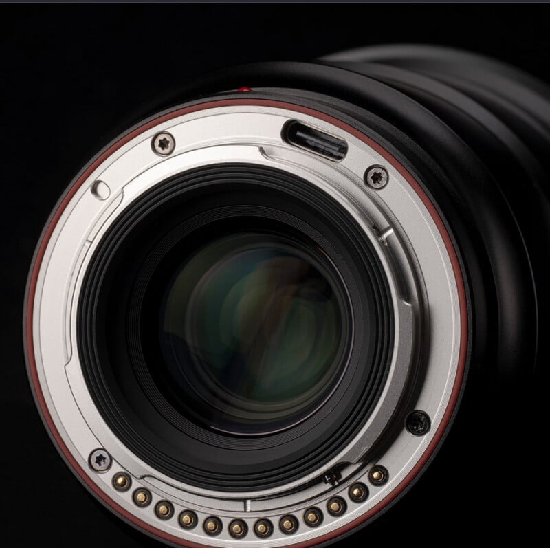 Close-up of a camera lens mount showing the metal contacts and surrounding details. The lens is set against a dark background, highlighting its reflective glass and intricate design components.