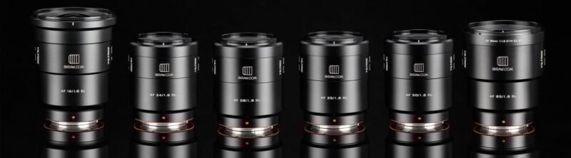 Six black camera lenses with varying focal lengths, arranged in a row against a black background. Each lens features a shiny metal mount at the base and has white text branding and specifications on the body.