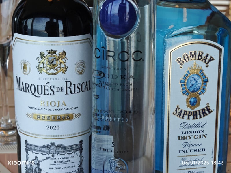 A close-up of three liquor bottles: Marques de Riscal Rioja wine, Cîroc vodka, and Bombay Sapphire gin. Labels showcase intricate designs and branding details, with a glass in the background. A Xiaomi camera watermark and timestamp are visible.