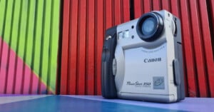 A Canon PowerShot 350 digital camera is displayed against a vibrant background with vertical red, green, and purple stripes.