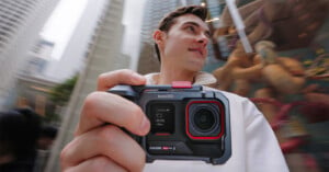 A person holding an Insta360 action camera, capturing a dynamic city scene. The background shows tall buildings and a blurred carousel. The person appears to be observing their surroundings with interest.