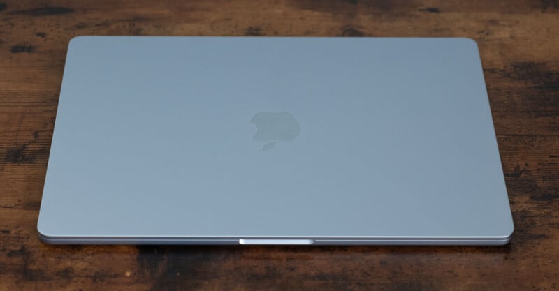 A closed silver laptop with an Apple logo on the back, resting on a wooden surface.