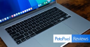 A silver laptop is open on a wooden surface, displaying a desktop screen with app icons. The keyboard and trackpad are visible. In the corner, there is an overlay with the words "PetaPixel Reviews.