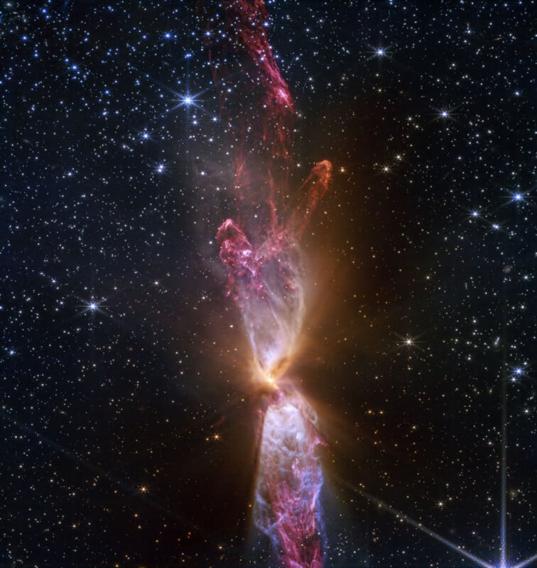 A dazzling space image shows a protostar emitting bright plumes of clouds and dust, forming an hourglass shape. Surrounding the protostar are myriad stars against a dark, starry background.