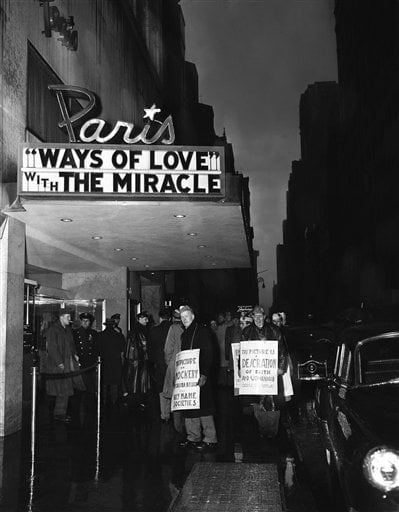 Black and white photo of Paris Theater showing "Ways of Love" on marquee. People holding protest signs stand on the sidewalk. The scene is set at night, and a car is parked nearby.