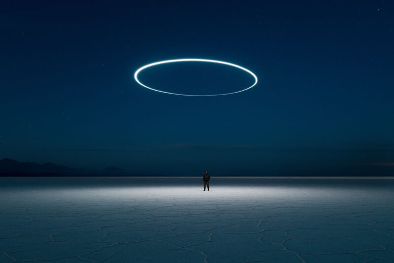 Uma pessoa fica em uma vasta superfície rachada sob um céu escuro e estrelado. Acima deles, uma luz circular brilhante paira, lançando uma iluminação estranha abaixo. O horizonte é levemente visível à distância.