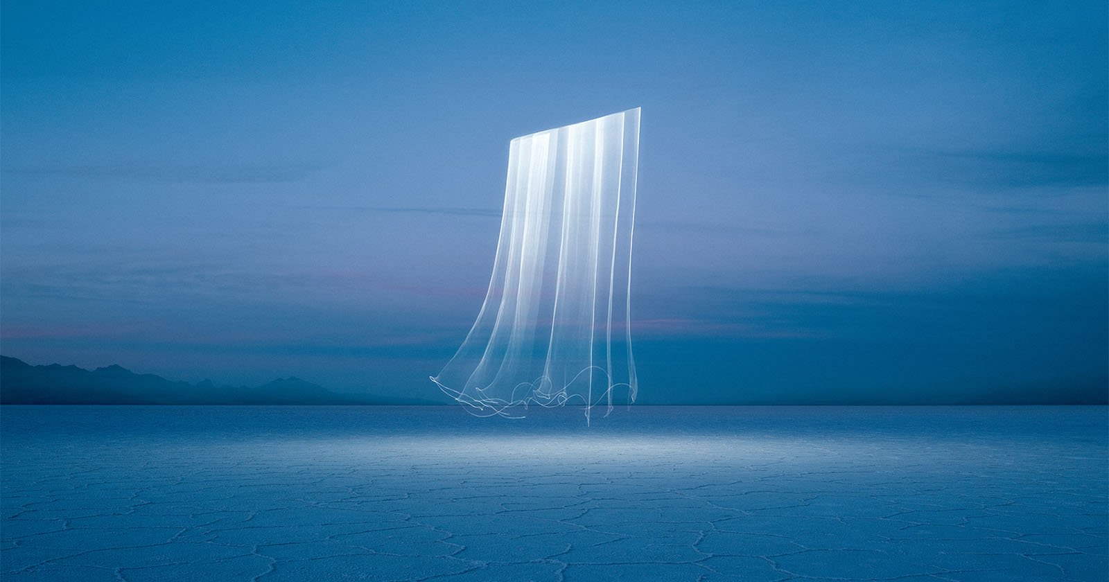 A surreal image shows a glowing, vertical light trail in the dusk sky over a vast, cracked salt flat. The cool blue tones create a mysterious atmosphere, with distant mountains visible on the horizon.