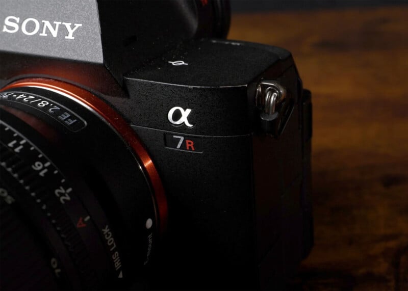 Close-up of a black Sony Alpha 7R camera with a lens attached, showing the camera's logo and model number on a wood-textured background.