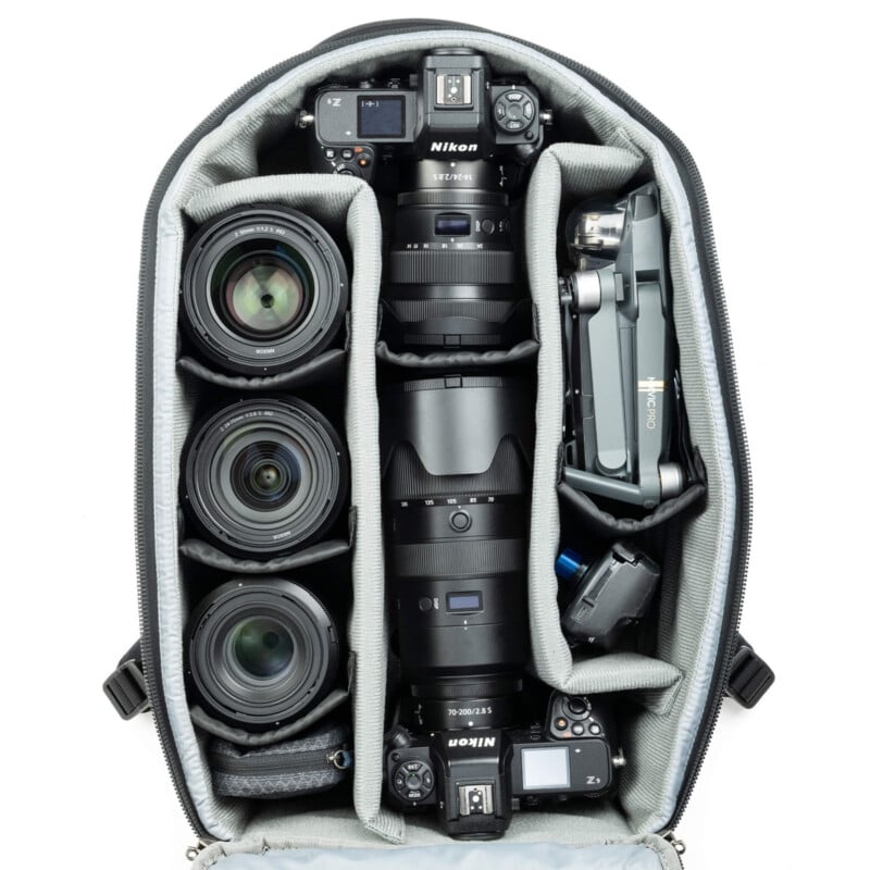 Top view of an open camera bag with neatly organized photography equipment, including multiple camera lenses, a drone, camera bodies, and other accessories in padded compartments.