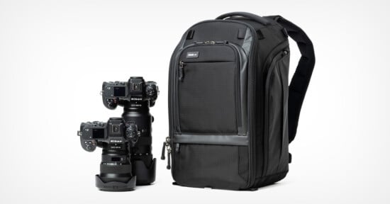 A black camera backpack next to two professional cameras with lenses attached. The backpack features zippers and several compartments for storage. The cameras are positioned upright, showcasing their lenses and bodies.