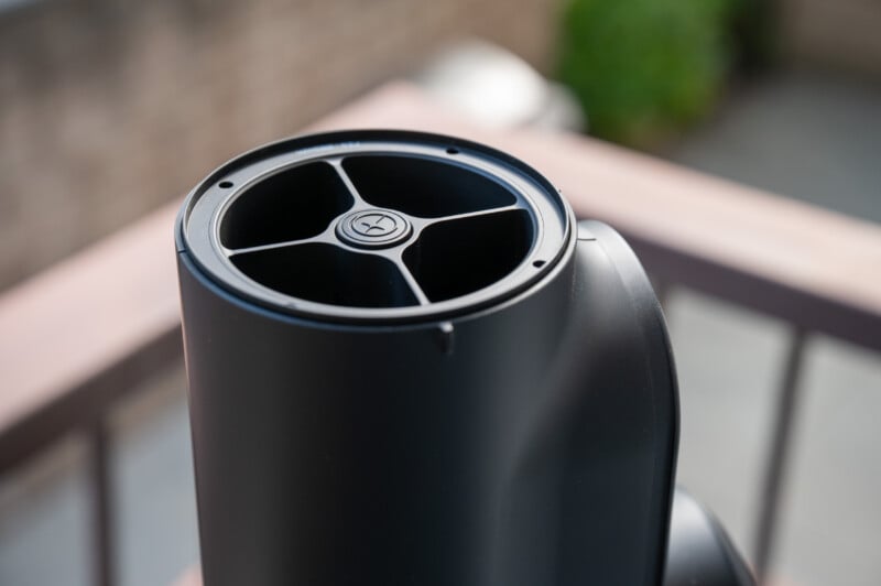 Close-up of the top section of a modern, black air purifier or fan with a circular vent and four curved spokes, positioned outdoors with a blurred background.