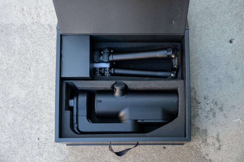 A black box with foam inserts containing a folded tripod, a camera gimbal, and an accessory box, all neatly organized, resting on a concrete surface.