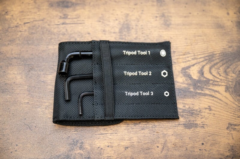 A black fabric pouch labeled "Tripod Tool 1," "Tripod Tool 2," and "Tripod Tool 3" holds three different L-shaped metal tools, laid on a wooden surface.