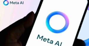 A hand holds a smartphone displaying the Meta AI logo, which features a blue and purple gradient circle, with the text "Meta AI" below it. The same logo and text appear in the image's top left corner.