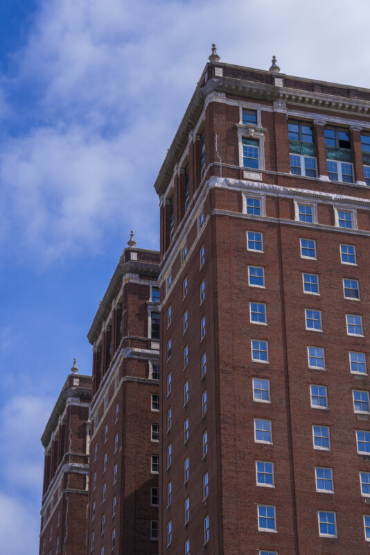 A tall, red-brick building with many windows reaches toward a partly cloudy blue sky. The architecture features decorative stone trim near the rooftop.