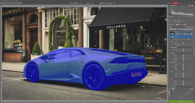 A sports car is parked on a city street in front of shops. The car is digitally highlighted in blue within a graphic editing software interface, displaying adjustment tools and color histograms on the right.