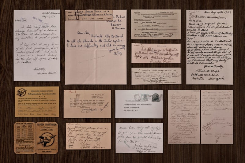 A collection of vintage handwritten letters, notes, and official documents arranged neatly on a wooden surface, including envelopes, postcards, and various types of stationery, showing aged paper and diverse handwriting styles.
