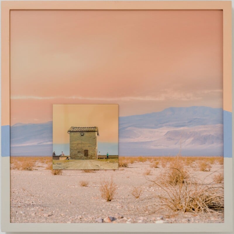 A framed image shows a desert landscape with dry grass and distant mountains. Within the frame, a smaller photo of a small house with people sitting outside is positioned in the center, blending into the background.