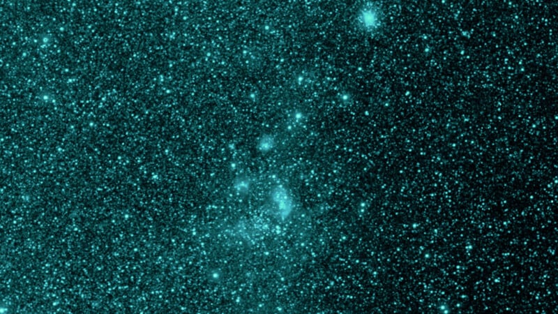 A dense field of teal-colored stars and cosmic dust fills the image, creating a textured, sparkling pattern against a dark background, resembling a starry night sky in space.