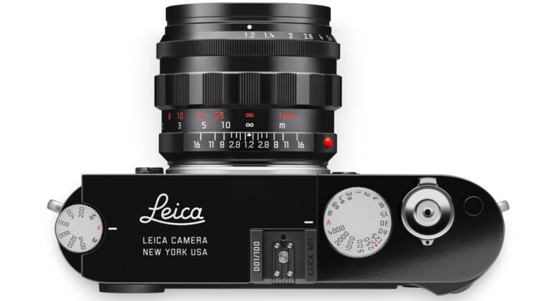 렌즈가 부착된 검은색 라이카 카메라를 위에서 본 모습입니다. 다이얼과 상단 플레이트에 "Leica Camera New York USA"라는 문구가 새겨져 있습니다. 렌즈에 초점과 조리개 표시가 보입니다.