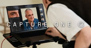A person using a laptop displaying portrait photos of an older man in editing software, with the words "CAPTURE ONE" overlaid on the image.