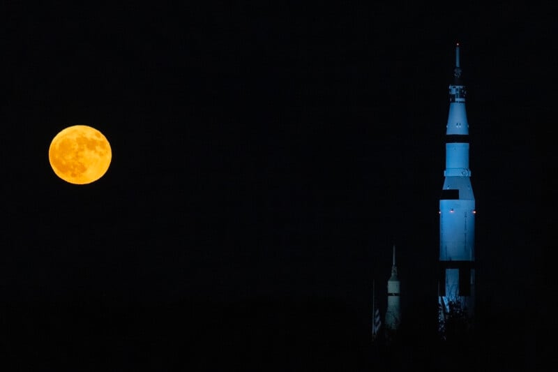 A large full moon glows in the night sky on the left, while a brightly lit, tall rocket stands on the right, silhouetted against the dark background.