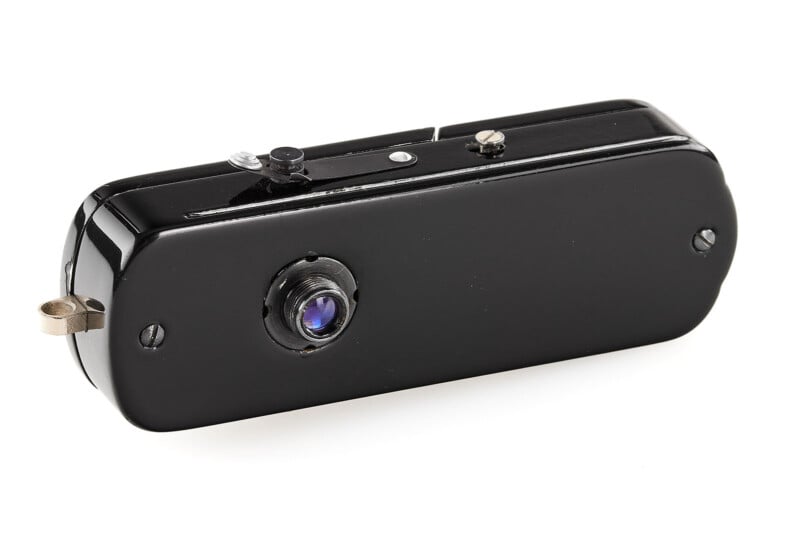 A compact, rectangular black vintage camera with a small round lens and simple controls on top, resembling a classic spy camera.