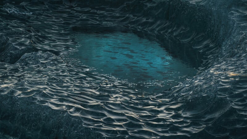 A close-up view of rippled blue ice forming a natural bowl around a pool of clear turquoise water, with textured, wavy ice surfaces reflecting light.