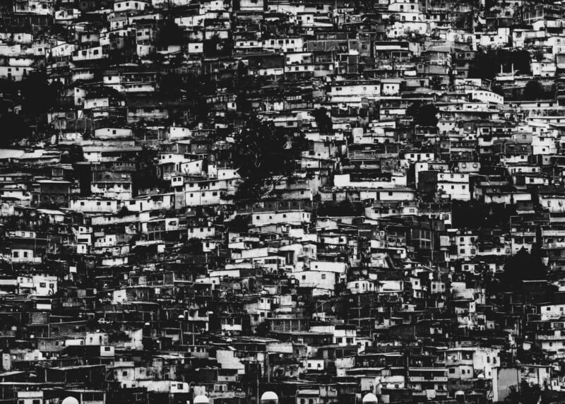 A densely packed hillside covered with small, tightly clustered houses. The image is in black and white, emphasizing the crowded and chaotic arrangement of the buildings.