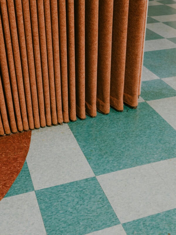 A brown, pleated room divider stands on a floor with green and white checkered tiles and a partial brown circle pattern in the bottom left corner.