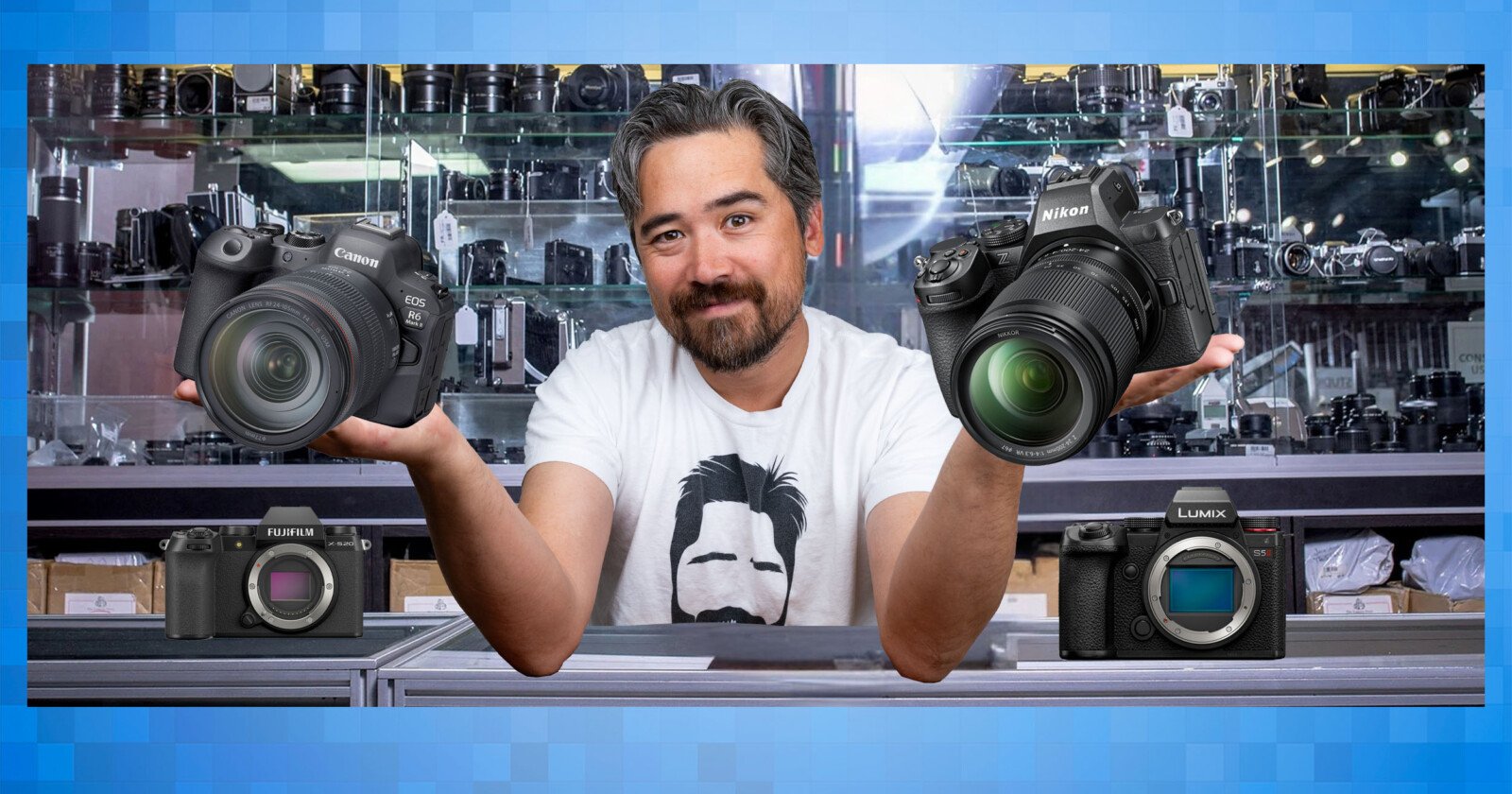 A man with a beard and mustache stands behind a counter in a camera shop, holding a Canon camera in one hand and a Nikon camera in the other. A Fujifilm and a Lumix camera are displayed in front of him.