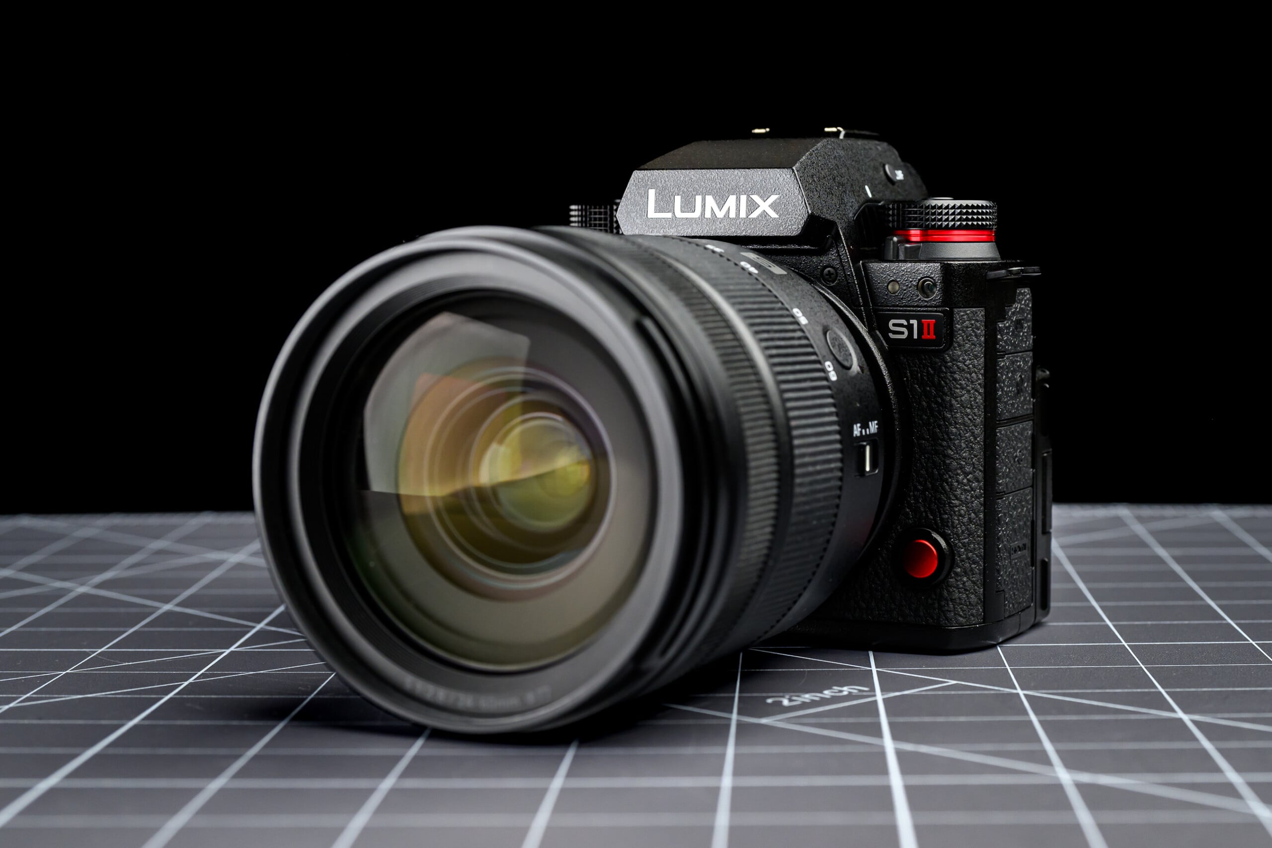 A Panasonic Lumix S1 II digital camera with a large lens is displayed on a grid-patterned surface, photographed against a black background.