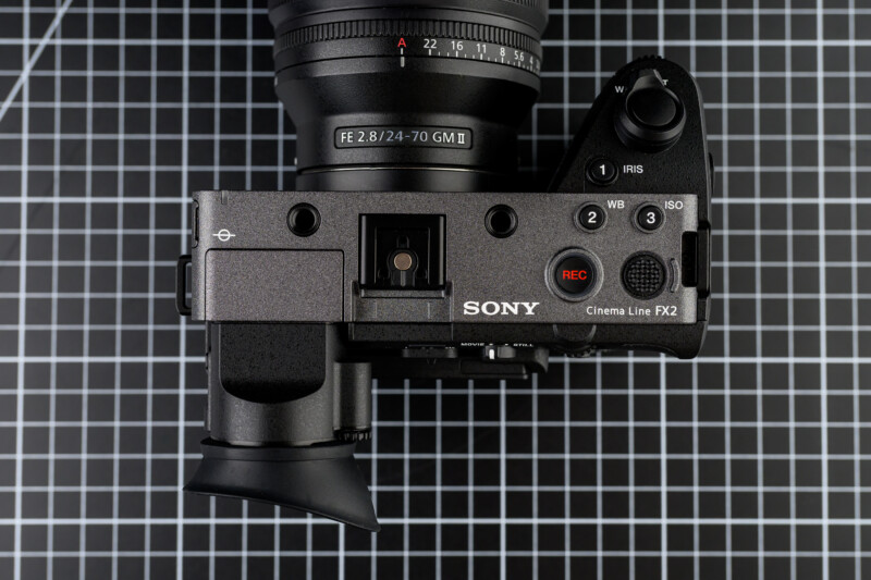 Top view of a Sony Cinema Line FX3 camera on a black and white grid background, showing various buttons, dials, and part of the attached FE 28-70mm GM lens.