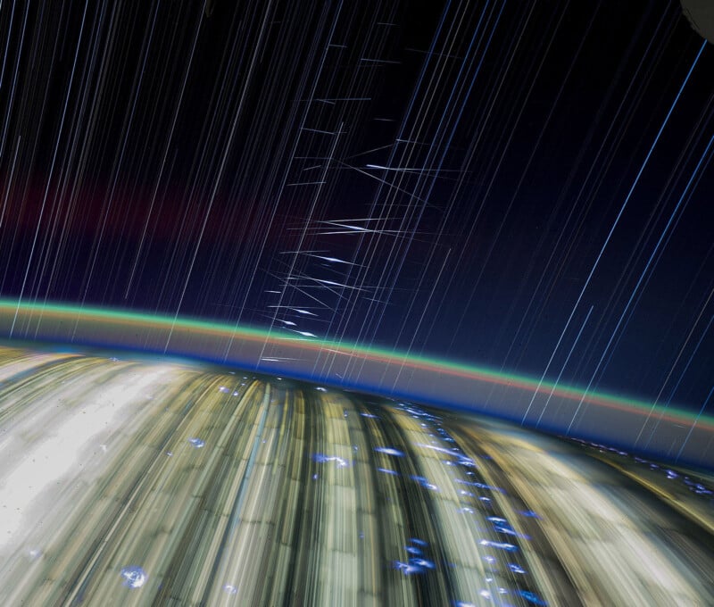 A time-lapse photo taken from space showing star trails in the dark sky, bright light streaks from Earth's surface, and a thin, colorful atmospheric layer along the curve of the planet.