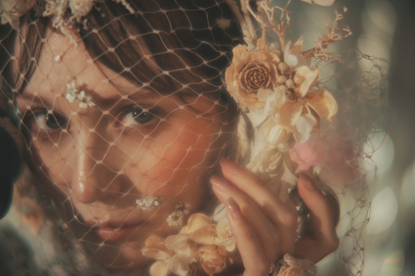 A person gazes through a delicate net veil adorned with dried flowers, gently touching the net with their fingers. The lighting is soft and dreamy, creating an ethereal and artistic mood.