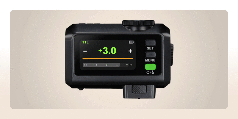 Close-up of a digital camera flash control unit displaying "+3.0" in green on its screen, with buttons labeled SET and MENU on the side, and a battery icon visible.